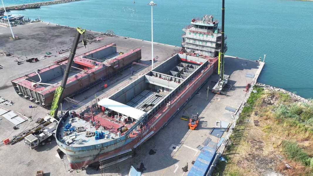 2000 dwt bulk carrier Aerial view of a red cargo ship being constructed or loaded with containers at a shipyard dock overlooking the sea.