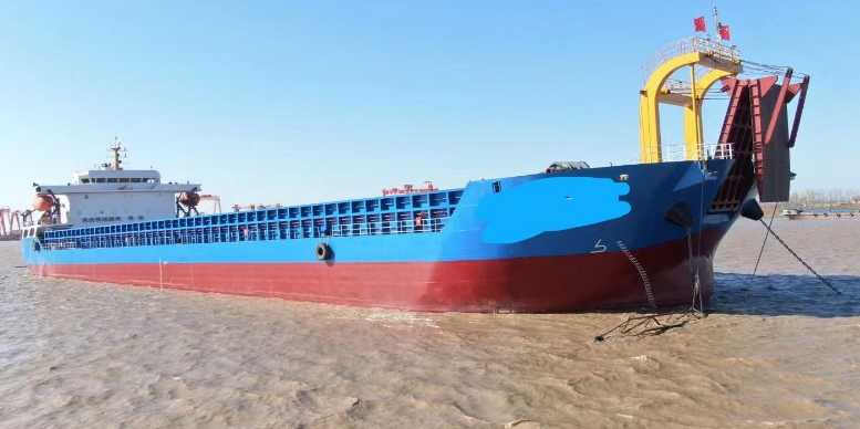 60m dock barge A blue and red bulk carrier ship docked along a muddy riverbank.