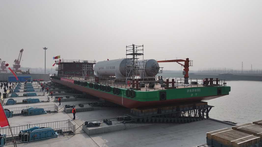 Bunkering barge A green barge carrying two tall white cylindrical tanks at a busy shipyard dock with cranes and workers.